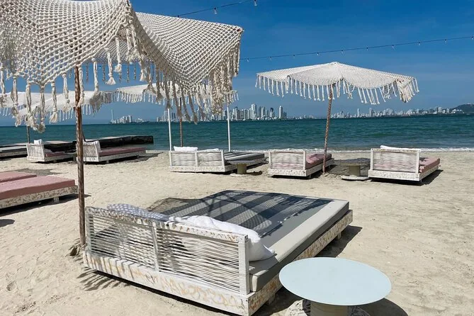 Fringed white parasols and daybeds on a sand beach with the Cartagena skyline across the water